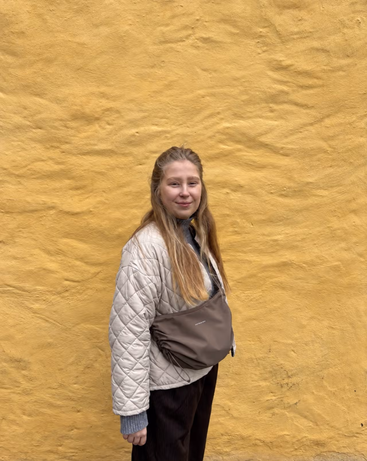 Nele steht vor einer senfgelben Wand und schaut in die Kamera
